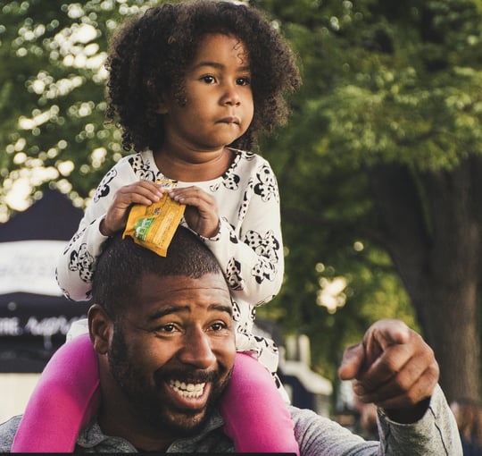 Smiling father giving his daughter a piggyback ride outdoors, enjoying playful time together in a park