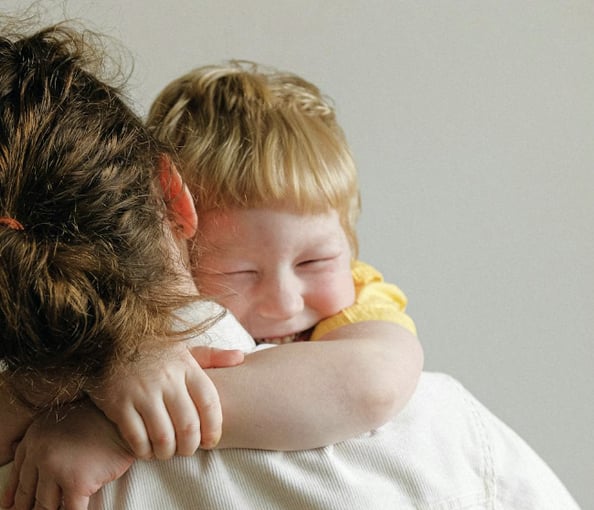 Smiling child hugging an adult, showing affection and emotional comfort in a warm, supportive environment