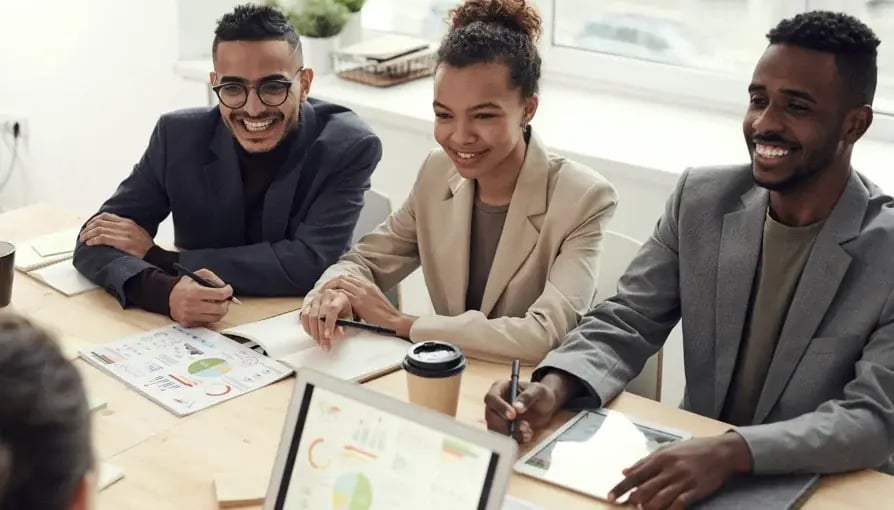 Three diverse professionals smile and engage during a collaborative meeting in an office setting.
