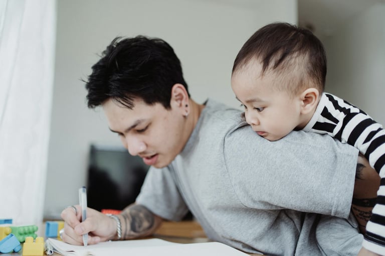 Father helping his young child with a drawing at a table, both focused and engaged in the activity