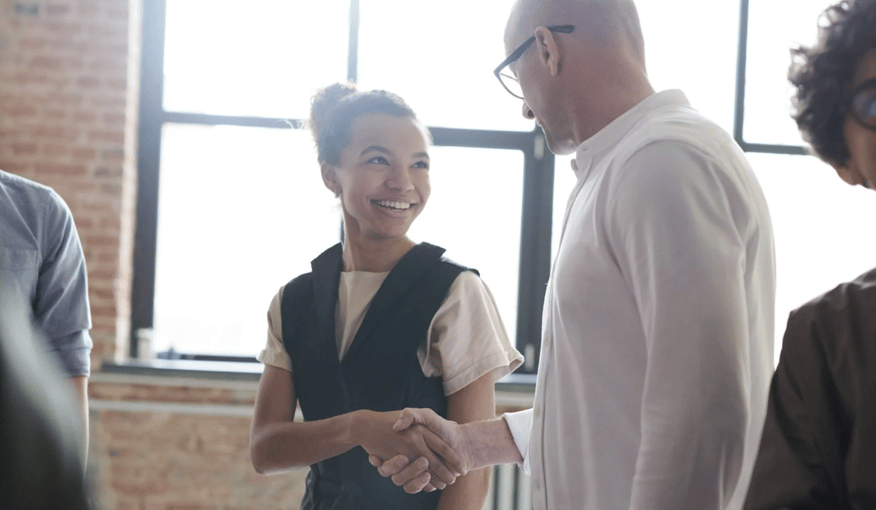Businesswoman smiling and shaking hands with a colleague in an office, symbolizing professional networking