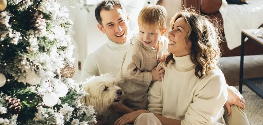 A family, including a child and a dog, celebrates Christmas in a cozy setting.
