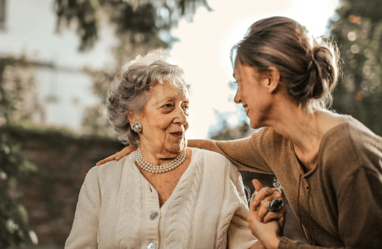 Smiling elderly woman and caregiver having a warm outdoor conversation, showing companionship and support
