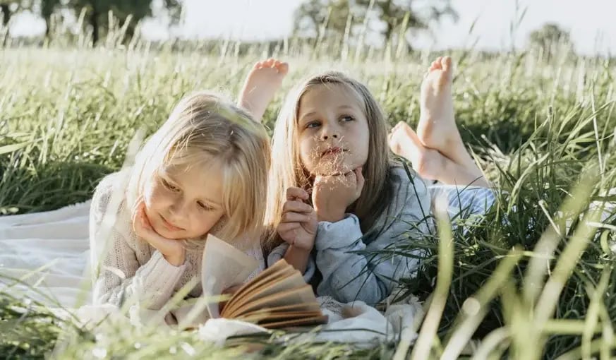 Two young girls lying in tall grass on a sunny day, enjoying a peaceful outdoor moment together