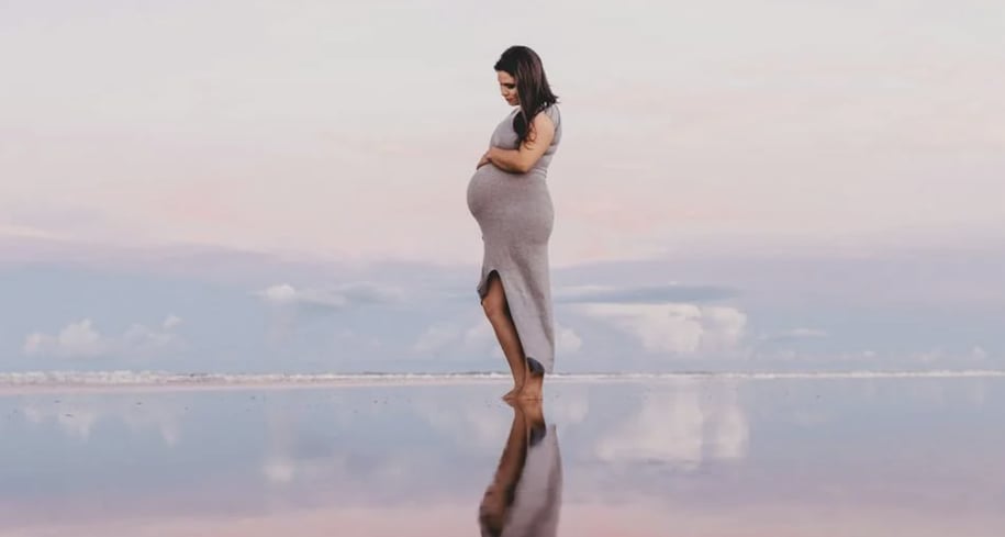A pregnant woman in a tight dress standing on a beach.
