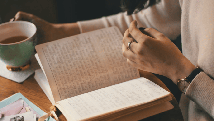 Person writing in a journal with a cup of tea nearby, creating a moment of reflection and self-care