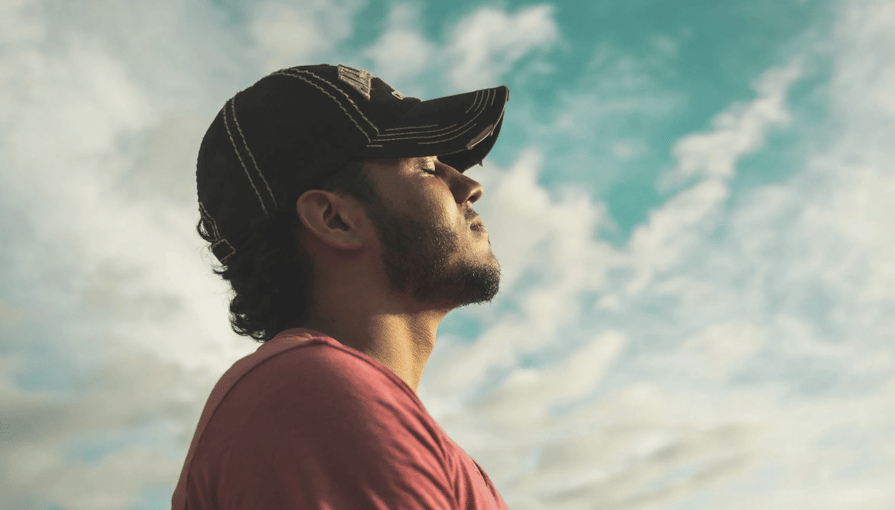 Man wearing a baseball cap looking up at a cloudy sky, appearing thoughtful and reflective