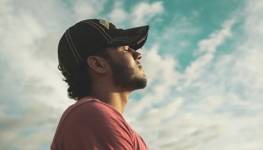 Man wearing a baseball cap looking up at a cloudy sky, appearing thoughtful and reflective