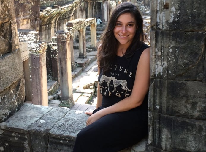 Woman sitting in front of ancient stone ruins, smiling and posing for a photo outdoors