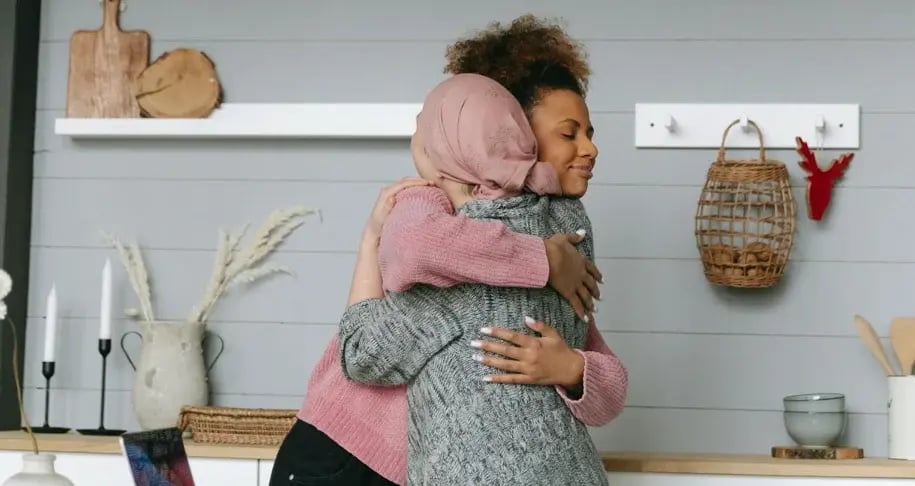 Two women embracing in a bright kitchen, sharing a supportive hug
